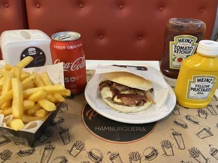 Porção de fritas ao lado de burger com bacon e lata de refrigerante, Pompéia's Burger