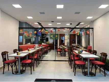 Salão com mesas brancas e cadeiras de assento vermelho